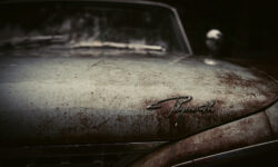 Close-up of a rusted hood of a car, with the logo "Plymouth" on it.